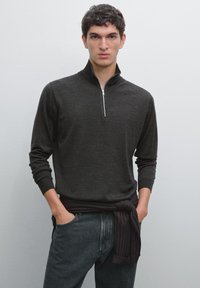 Dark grey pullover sweater with a half-zip collar, long sleeves, and ribbed cuffs, paired with dark denim jeans and a dark fabric tied at the waist.