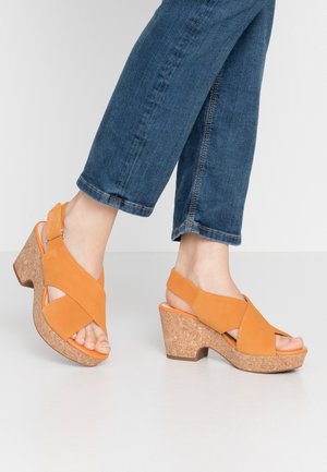 Sandali a zeppa in suede arancione con cinturini incrociati e zeppa in sughero. Presentano un design open toe e una cinghia sul tallone per un supporto extra.