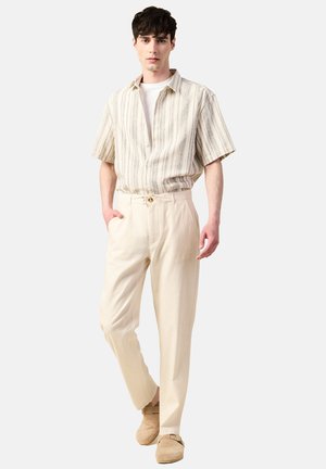 Crème kleurige linnen broek met een ontspannen pasvorm, voorzien van een trekkoord in de taille en voordoekjes. Gecombineerd met een gestreept shirt met korte mouwen.