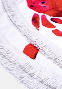 White towel featuring a red and pink abstract design. Edged with decorative white fringe for added texture and detail.