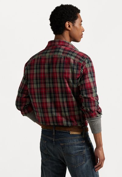 Camisa de franela a cuadros en rojo y azul marino con puños grises, cuello abotonado y corte relajado. Llevada con jeans de mezclilla oscuros.