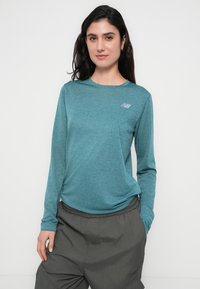 Τιρκουάζ αθλητικό πουκάμισο με μακριά μανίκια από ελαφρύ υλικό, με στρογγυλή λαιμόκοψη και μικρό ανακλαστικό λογότυπο στο στήθος.