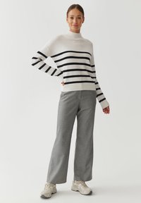 Pull rayé blanc avec des rayures noires, col montant, associé à un pantalon ample gris et des baskets beiges. Texture de tissu lisse.