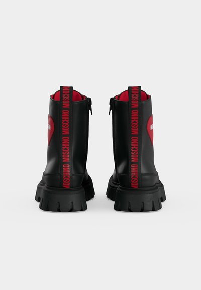 Bottines en cuir noir à semelles épaisses, détail cœur rouge sur les côtés, et "MOSCHINO" imprimé en rouge sur les languettes à l’arrière.