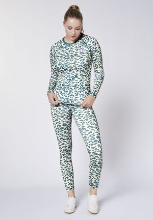 Woman wearing matching long-sleeve top and leggings with blue and white leopard print, standing against a plain light background.
