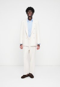 White double-breasted suit jacket over a light blue shirt with long sleeves, paired with matching trousers and dark brown loafers.