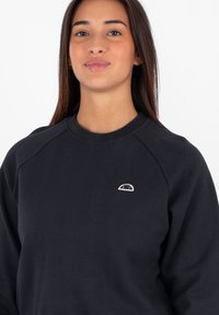 Felpa nera con scollo rotondo e maniche raglan. Presenta un piccolo logo ricamato in colori chiari sul petto. Texture liscia.