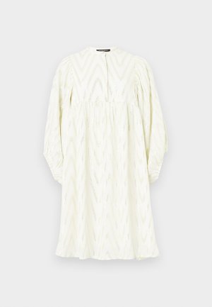 Bijela haljina s visokim ovratnikom, dugim napuhanim rukavima i cik-cak uzorkom. Izrađena od teksturirane tkanine s suptilnim metalnim akcentima.