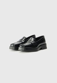 Sorte skinnloafers med en glanset finish, som har et forhøyet aksentbånd og en kraftig, lett hevet såle.