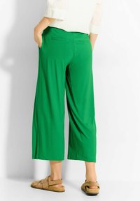 Zielone, szerokie spodnie wykonane z miękkiego materiału, z bocznymi kieszeniami, luźnym krojem i średnim stanem. Zauważalne detale przeszycia na kieszeniach.