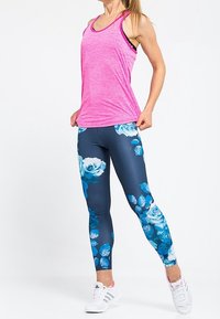 Canotta atletica rosa, abbinata a leggins blu con un motivo floreale blu; modello che indossa scarpe da ginnastica bianche.