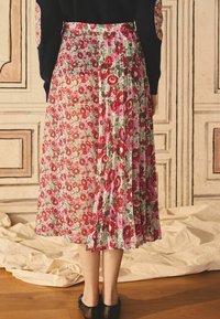 Jupe midi florale avec des motifs multicolores de rouge, rose et vert. Design plissé avec une taille ajustée, faite en tissu léger.