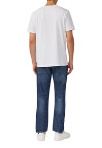 T-shirt bianco a maniche corte, vestibilità comoda, realizzato in cotone. Abbinato a jeans in denim blu, gamba dritta, e sneakers bianche. Design semplice.