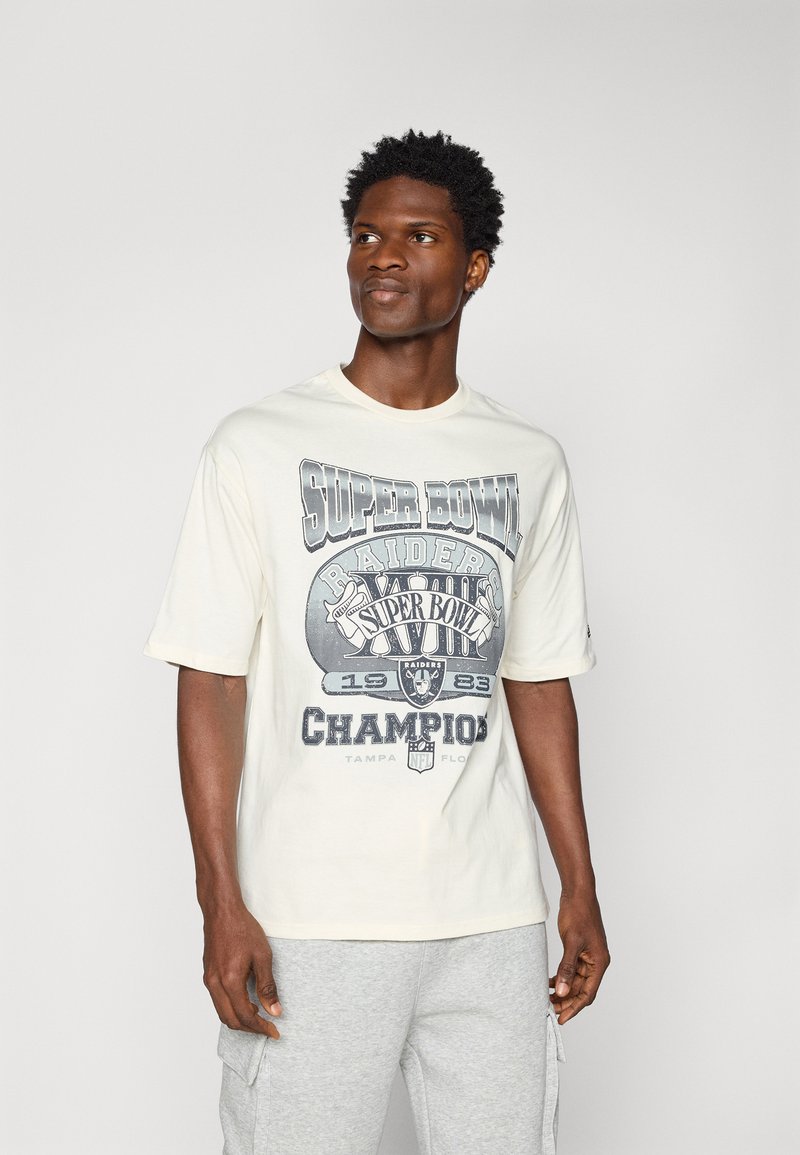 Camiseta de algodón blanca con un estampado gráfico desgastado de "Super Bowl Raiders Campeones 1983" en gris, de mangas cortas y diseño de cuello redondo.