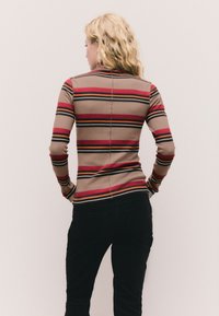 Garām piedurknēm tops no stiepjoša auduma ar horizontālām svītrām brūnā, sarkanā un melnā krāsā. Mugurpusei ir augsta apkakle un piegulošs dizains.