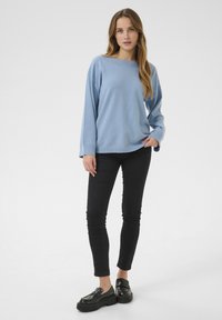 Maglione oversized azzurro chiaro con scollatura ampia, maniche lunghe e polsini a coste, abbinato a jeans skinny neri e mocassini neri con plateau.