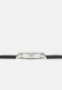 Montre en acier inoxydable argenté avec un bracelet en cuir noir, cadran rond et couronne du côté droit. Design minimaliste avec une finition lisse.