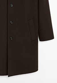 Cappotto di lana marrone scuro con taglio dritto, dotato di bottoni neri e una tasca laterale. Tessuto morbido, design minimalista e senza motivi visibili.