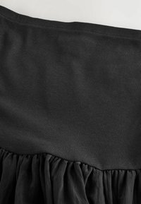 Gros plan d’un vêtement noir montrant une ceinture côtelée en tricot et un tissu léger froncé sous la couture de la taille.