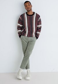 Striped knit sweater with maroon, cream, and gray tones, paired with light green corduroy pants and white footwear. Casual fit, textured materials.