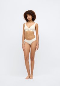 Σετ εσωρούχων σε ανοιχτό μπεζ απόχρωση, που περιλαμβάνει ένα μπραλέτ με δαντελένια λεπτομέρεια και φιόγκο, συνδυασμένο με αντίστοιχα μπικίνι. Λείος υφασμάτινος τύπος.