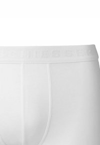 Boxer de algodón blanco con cintura elástica texturizada que muestra el nombre de la marca en relieve, tela suave y diseño ajustado.