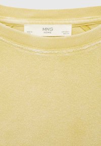 Gul sweatshirt med en texturerad tyg, ribbad halsringning och etikett märkt "MNG HOME." Sömmar synliga runt kragen.