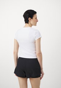 Weißes Kurzarmoberteil mit rundem Halsausschnitt, kombiniert mit schwarzen Shorts. Das Material wirkt glatt und eng anliegend, mit minimalen Nähten.