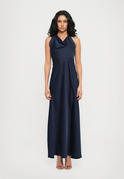 Marineblaue Maxikleid mit Neckholder und drapiertem Vorderteil. Glatter Stoff, tailliertes Oberteil und fließender Rock. Kombiniert mit hellen Riemchenabsätzen.