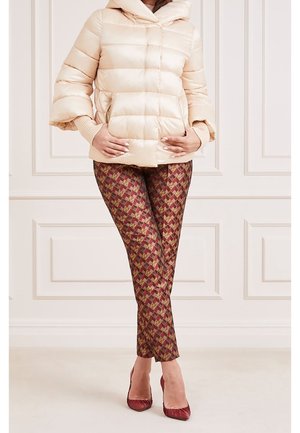 Béžová vatovaná bunda s kapucí a žebrovanými manžetami, kombinovaná s legínami vzorovanými v burgundské a zlaté barvě. Modelka má na nohou odpovídající červené podpatky.