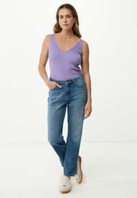Liliowa, żeberkowana koszulka na ramiączkach zestawiona z jasnoniebieskimi prostymi jeansami. Modelka ma na sobie białe sneakersy. Tło jest gładkie, białe.