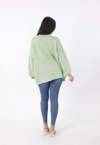Hellgrüner, übergroßer Strickpullover mit überschnittenen Schultern, langen Ärmeln und geripptem Ausschnitt. Kombiniert mit blauen Skinny-Jeans und klaren Blockabsätzen.