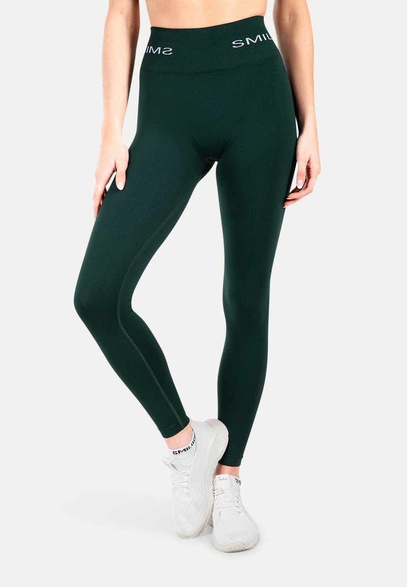 Leggings verde scuro con una cintura alta che presenta il marchio "SMIL". Il materiale ha una finitura liscia, offrendo flessibilità e comfort.