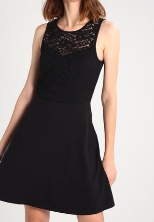 Czarna sukienka z koronkowym górnym fragmentem i gładkim dołem. Bez rękawów, z zaokrąglonym dekoltem. Gładka faktura na całej powierzchni.