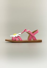 Ροζ παιδικό σανδάλι με μεγάλη λευκή και κίτρινη μαργαρίτα διακοσμητική, λουράκι με αγκράφα και επίπεδη καφέ σόλα σε ουδέτερο φόντο.
