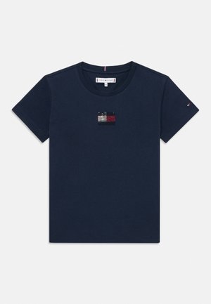 T-shirt en coton bleu marine avec un petit logo texturé sur la poitrine en blanc, rouge et noir. Manches courtes et col rond.