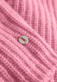 Różowy sweter dzianinowy o prążkowanej fakturze i okrągłym srebrnym guziku z sylwetką czerwonego psa. Miły i przytulny wygląd.