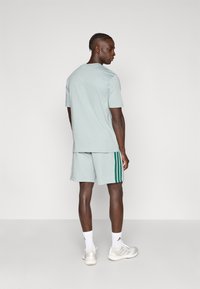 Ανοιχτό πράσινο αθλητικό σύνολο με μπλούζα κοντομάνικη και στρογγυλή λαιμόκοψη και ταιριαστό σορτς με σκούρες πράσινες ρίγες στα πλάγια. Αθλητικά παπούτσια σε ουδέτερο χρώμα.