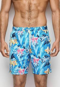 Los pantalones de baño florales azules presentan una mezcla de grandes flores rosas y amarillas con hojas verdes, una cinturilla con cordón y una tela suave y liviana.