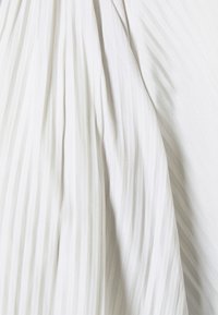 Tissu blanc avec des plis verticaux sur le côté gauche se fondant dans une texture lisse et légèrement froissée sur le côté droit.