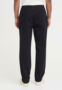 Pantalones de algodón negros con un corte relajado, que cuentan con dos bolsillos traseros, cinturilla elástica y piernas ligeramente ajustadas. Textura suave.