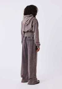 Sudadera gris recortada con capucha y pantalones grises de pierna ancha. Tejido suave y texturizado con costuras visibles y bolsillos laterales.