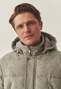 Hall halliga isoleeritud jakk kõrge kraega, kahe tõmblukuga taskuga ja eemaldatava kapuutsiga. Pehme tekstuur ja tikitud disain soojuse tagamiseks.