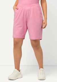 Shorts di cotone rosa con vita elastica, tasche laterali e vestibilità comoda, abbinati a sneakers bianche sportive.