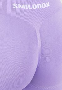 Zbliżenie na lawendowe legginsy sportowe z wyraźnym pasem oznaczonym napisem "SMILODOX", podkreślające teksturę i dopasowanie.