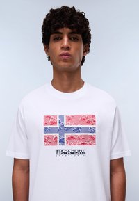 White cotton t-shirt featuring a stylized Norwegian flag graphic in red and blue with wavy lines, and "NAPAPIJRI geographic" text below.