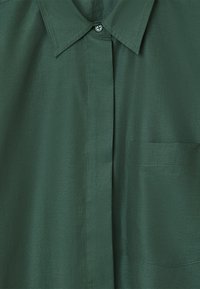 Dark green button-up shirt featuring a classic collar, pocket on the left side, smooth texture, and subtle sheen.
