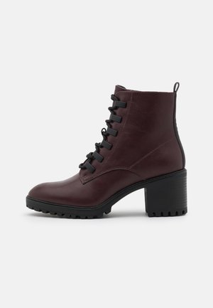 Bottine en cuir marron foncé avec talon bloc épais, devant à lacets noirs et languette à l'arrière.