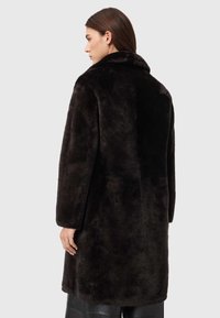 Casaco de pelo sintético escuro com textura macia, apresentando uma gola larga e mangas compridas, terminando ao meio da coxa. Design simples sem detalhes adicionais.