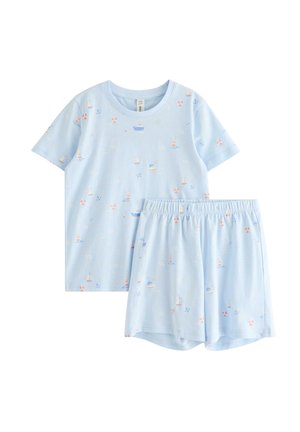 Uśmiechnięte bose dziecko z długimi blond włosami, ubrane w jasnoniebieską pasującą koszulę i krótkie spodenki z małymi kolorowymi nadrukami o tematyce morskiej.